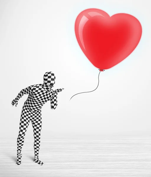 Cute guy in morpsuit body suit looking at a balloon shaped heart — Stock Photo, Image