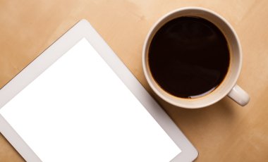 Boş alanı olan bir tablet bilgisayar ve masada bir fincan kahve.