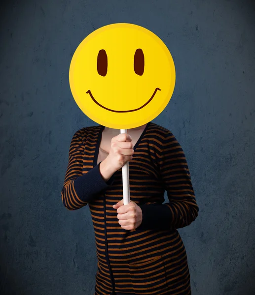 Mujer joven sosteniendo un emoticono sonriente —  Fotos de Stock