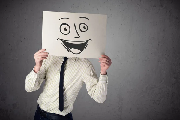 Empresário segurando um papelão com rosto sorridente na frente — Fotografia de Stock