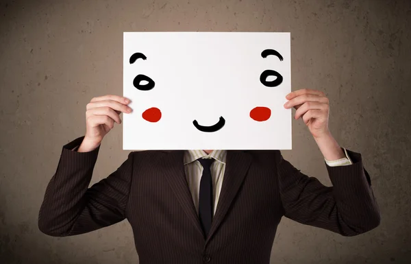 Businessman holding a cardboard with a smiley face on it — Stock Photo, Image