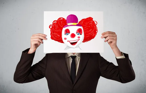 Businessman holding a cardboard with a clown on it in front of h — Stock Photo, Image