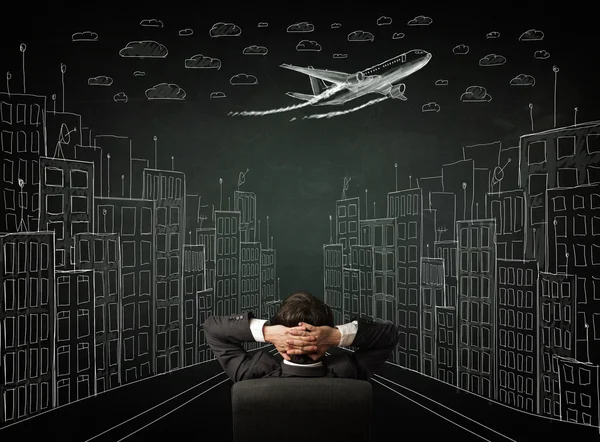 Businessman sitting in front of a cityscape drawing on a chalkbo — Stock Photo, Image