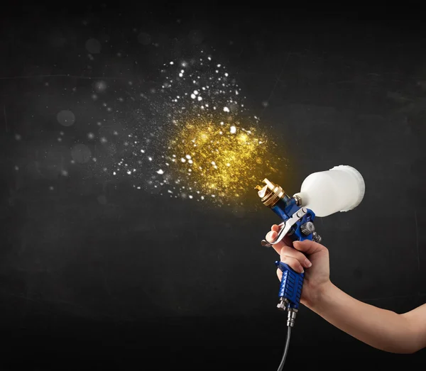 Worker with airbrush painting with glowing golden paint — Stock Photo, Image