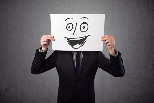 Businessman holding a cardboard with smiley face on it in front — Stock Photo, Image