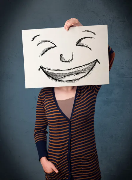 Frau mit gezeichnetem Smiley-Gesicht auf einem Papier vor ihrem Kopf — Stockfoto