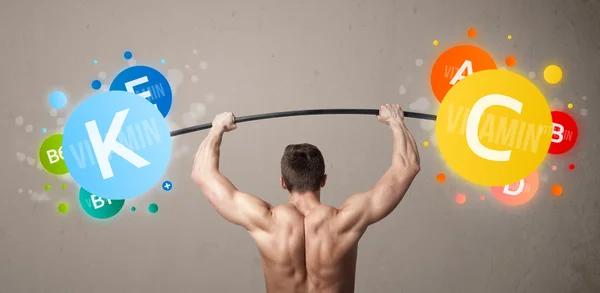 Muscular man lifting colorful vitamin weights — Stock Photo, Image