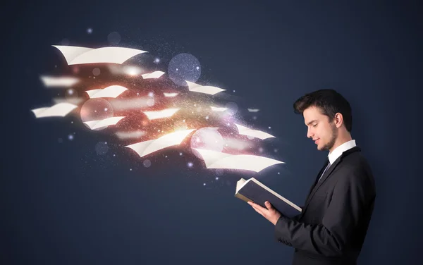 Young guy reading a book with flying sheets coming out of the bo — Stock Photo, Image