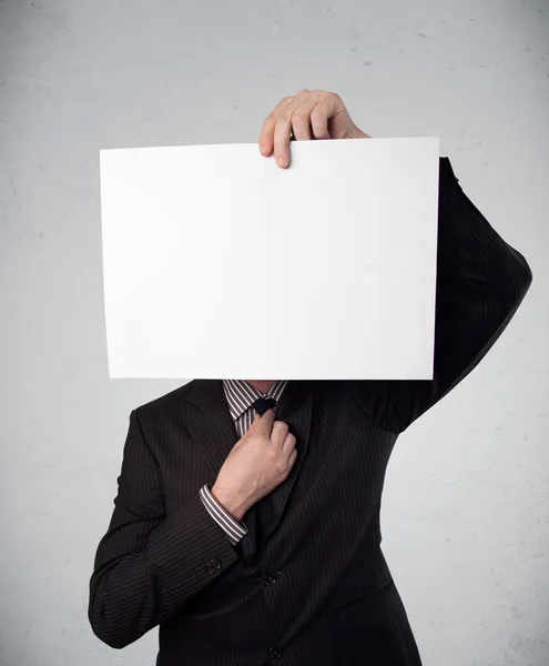 Empresario sosteniendo delante de su cabeza un papel con espacio para copias —  Fotos de Stock