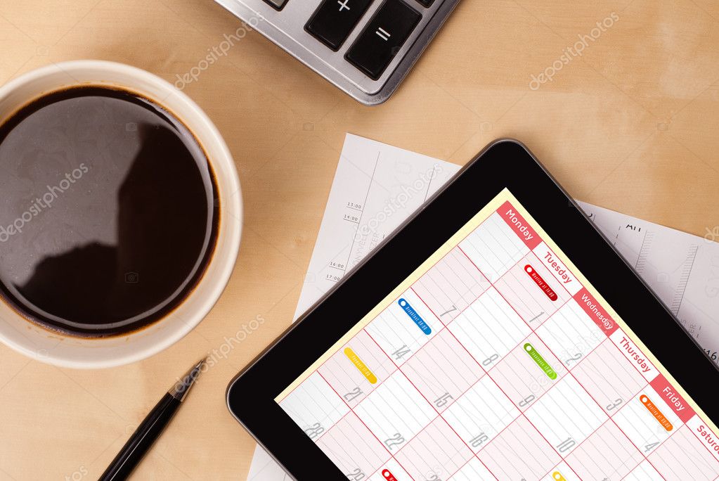 Tablet pc showing calendar on screen with a cup of coffee on a d