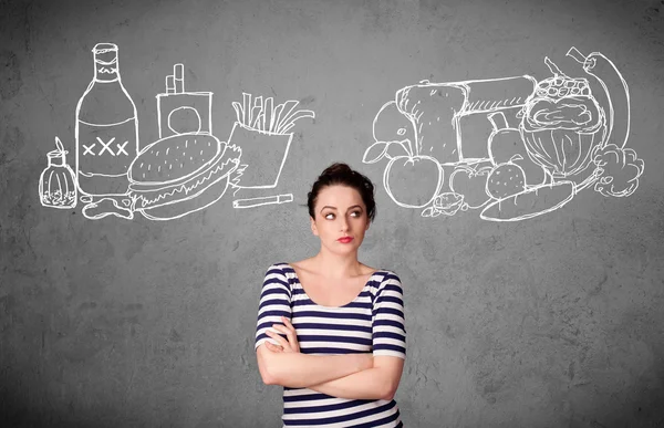 Woman standing between healthy and unhealthy foods — Stock Photo, Image