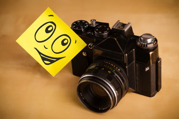 Post-it note with smiley face sticked on photo camera — Stock Photo, Image