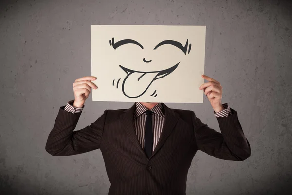 Businessman holding a paper with funny smiley face in front of h — Stock Photo, Image