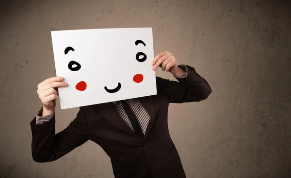 Businessman holding a cardboard with a smiley face on it — Stock Photo, Image