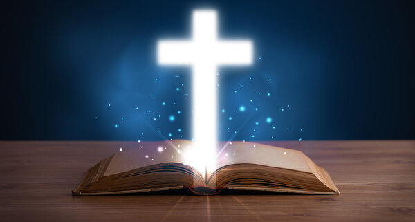 Open holy bible with glowing cross in the middle