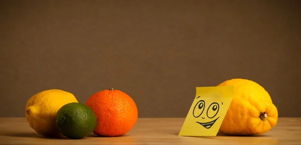 Lemon with post-it note looking at citrus fruits — Stock Photo, Image