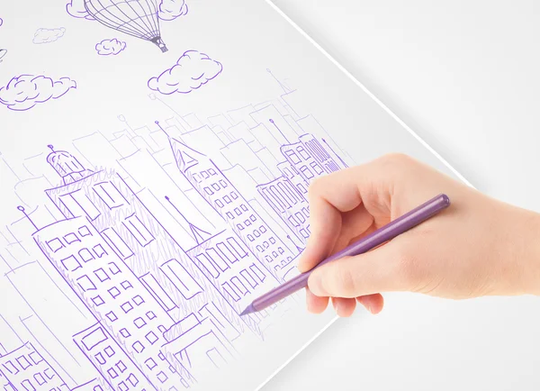 Eine Person zeichnet eine Skizze einer Stadt mit Luftballons und Wolken auf einem — Stockfoto
