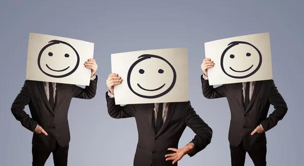 Hombres de traje haciendo gestos con caras sonrientes dibujadas en cartón — Foto de Stock