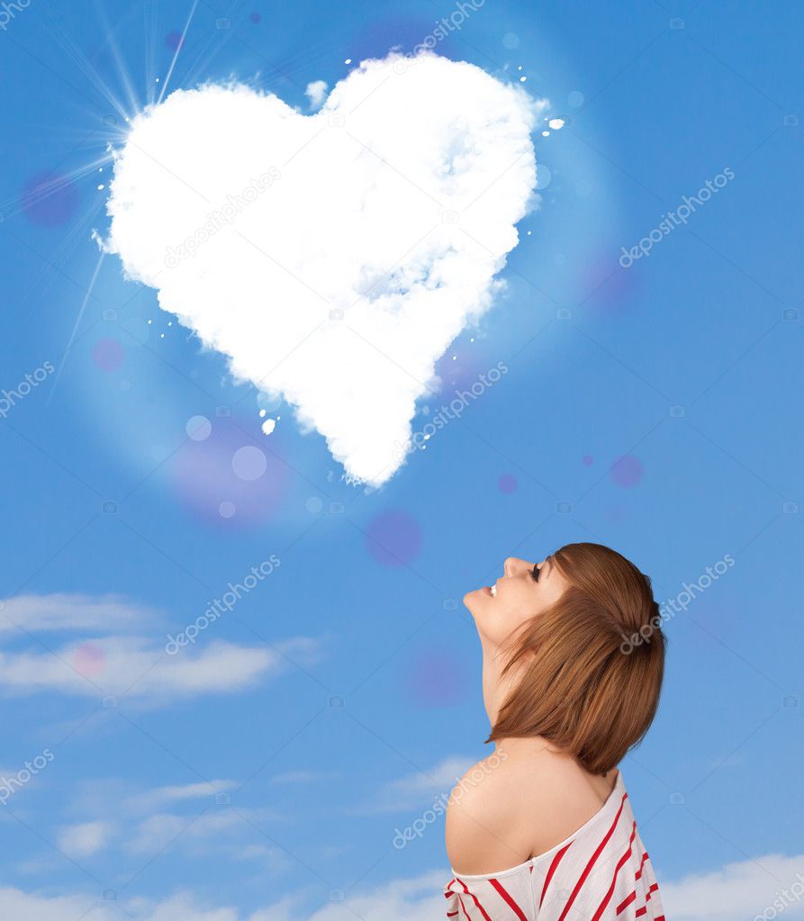 Cute girl looking at white heart cloud on blue sky