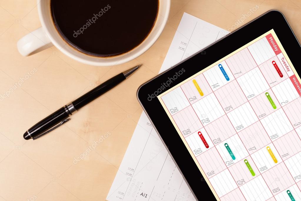 Tablet pc showing calendar on screen with a cup of coffee on a d