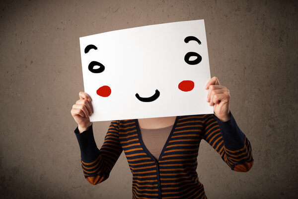 Woman holding a cardboard with a smiley face on it