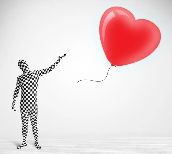 Cute guy in morpsuit body suit looking at a balloon shaped heart — Stock Photo, Image