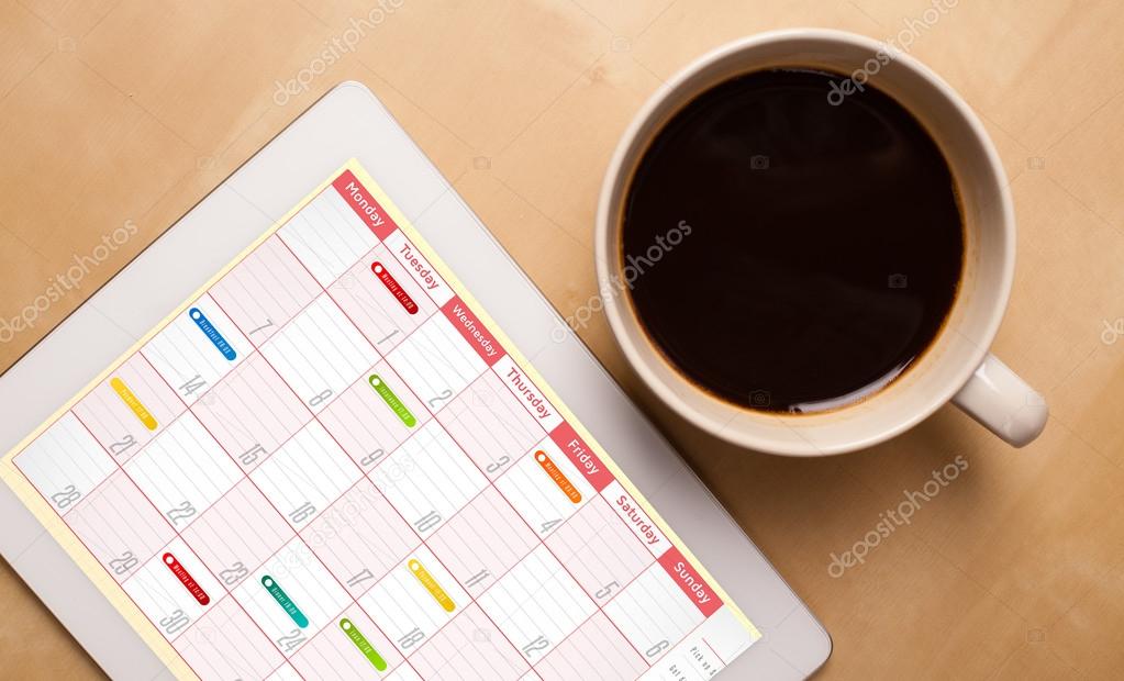 Tablet pc showing calendar on screen with a cup of coffee on a d