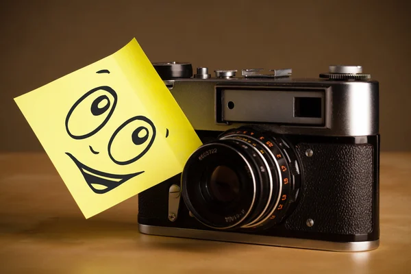 Post-it opmerking met smileygezicht gevezen op fotocamera — Stockfoto