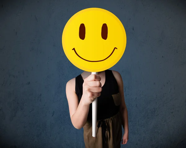 Young woman holding a smiley face emoticon — Stock Photo, Image