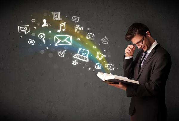 Joven hombre de negocios leyendo un libro con iconos multimedia — Foto de Stock