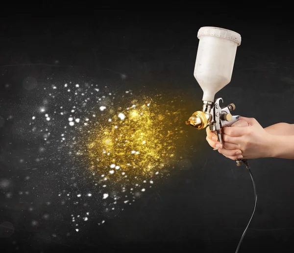 Worker with airbrush painting with glowing golden paint — Stock Photo, Image