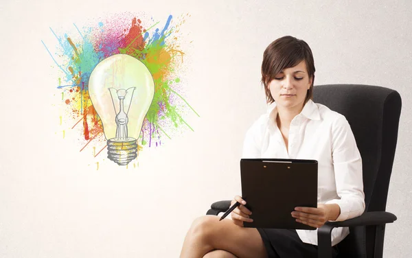 Young lady drawing a colorful light bulb with colorful splashes — Stock Photo, Image