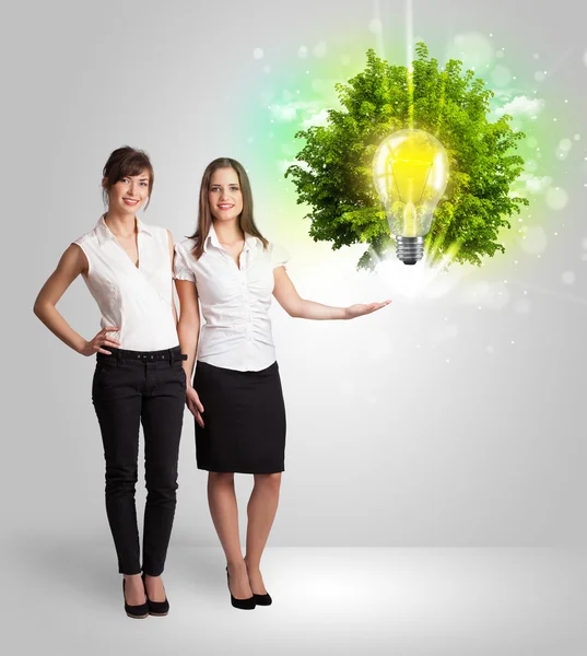 Young girl presenting idea light bulb with green tree — Stock Photo, Image