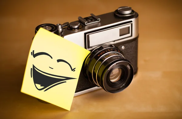 Nota pós-it com rosto sorridente colado na câmera fotográfica — Fotografia de Stock