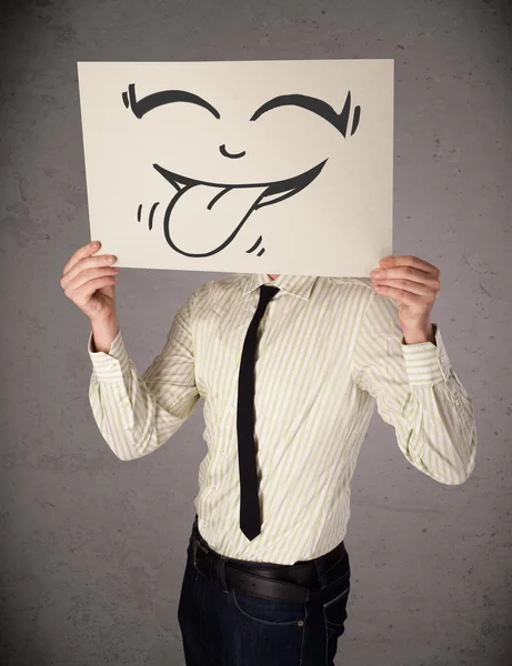 Businessman holding a paper with funny smiley face in front of h — Stock Photo, Image