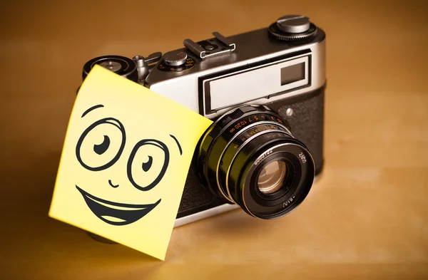 Post-it opmerking met smileygezicht gevezen op fotocamera — Stockfoto