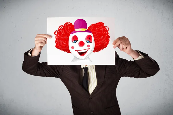 Бизнесмен держит картон с клоуном на нем перед h — стоковое фото