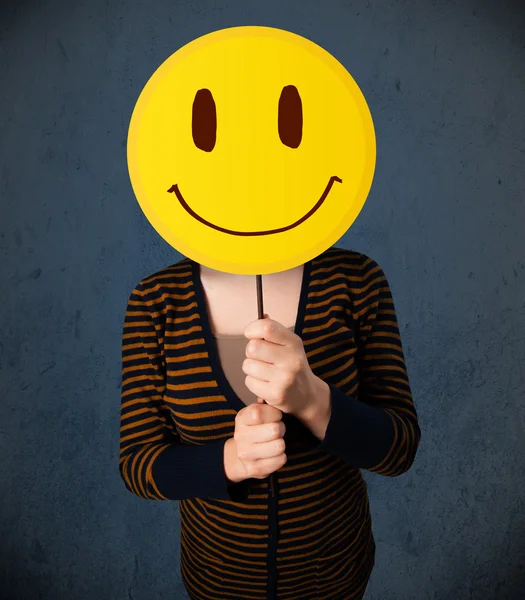 Jovem mulher segurando um emoticon rosto sorridente — Fotografia de Stock