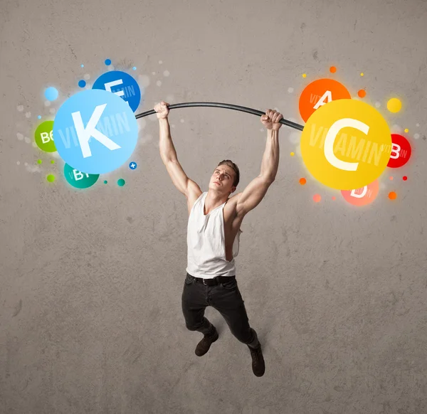 Muscular man lifting colorful vitamin weights — Stock Photo, Image