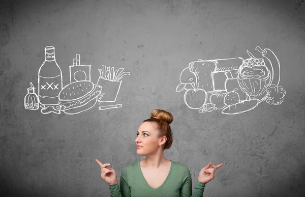 Woman standing between healthy and unhealthy foods — Stock Photo, Image