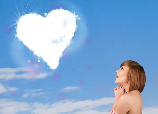Симпатичная девушка смотрит на белое сердце облако на голубом небе — стоковое фото