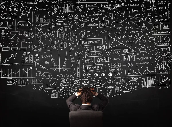 Businessman sitting in front of a blackboard with charts — Stock Photo, Image