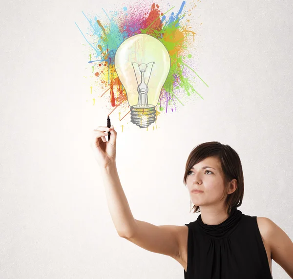 Young lady drawing a colorful light bulb with colorful splashes — Stock Photo, Image