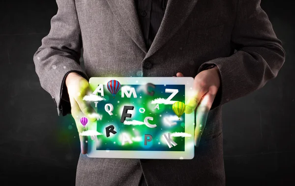 Young person showing tablet with abstract letters and sky — Stock Photo, Image