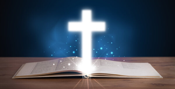 Open holy bible with glowing cross in the middle