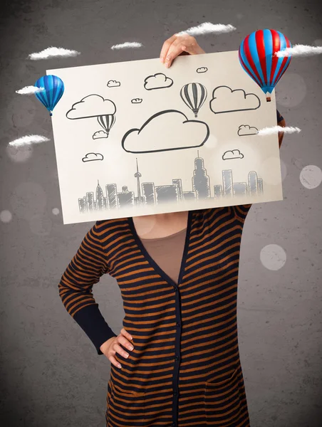 Femme tenant un carton avec paysage urbain devant sa tête — Photo