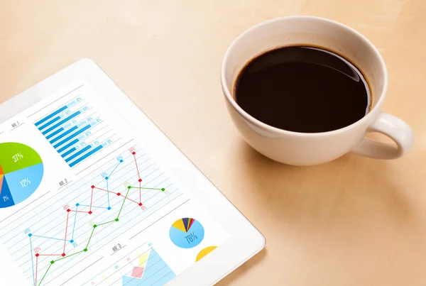 Tabletpc toont grafieken op het scherm met een kopje koffie op een bureau — Stockfoto