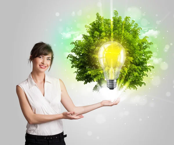 Young girl presenting idea light bulb with green tree — Stock Photo, Image