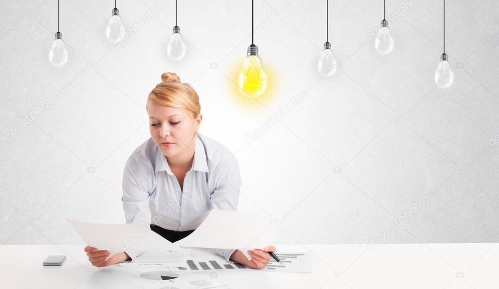 Business woman sitting at table with idea light bulbs