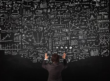 İşadamı tahtaya çizilmiş çizelgelerin önünde duruyor.